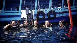 Five PADI Open Water divers on the sea surface smiling while the boat waiting behind them