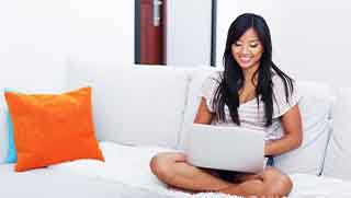 Black hair smiling women sitting home on a white sofa reading PADI Open Water diver manual from a tablet